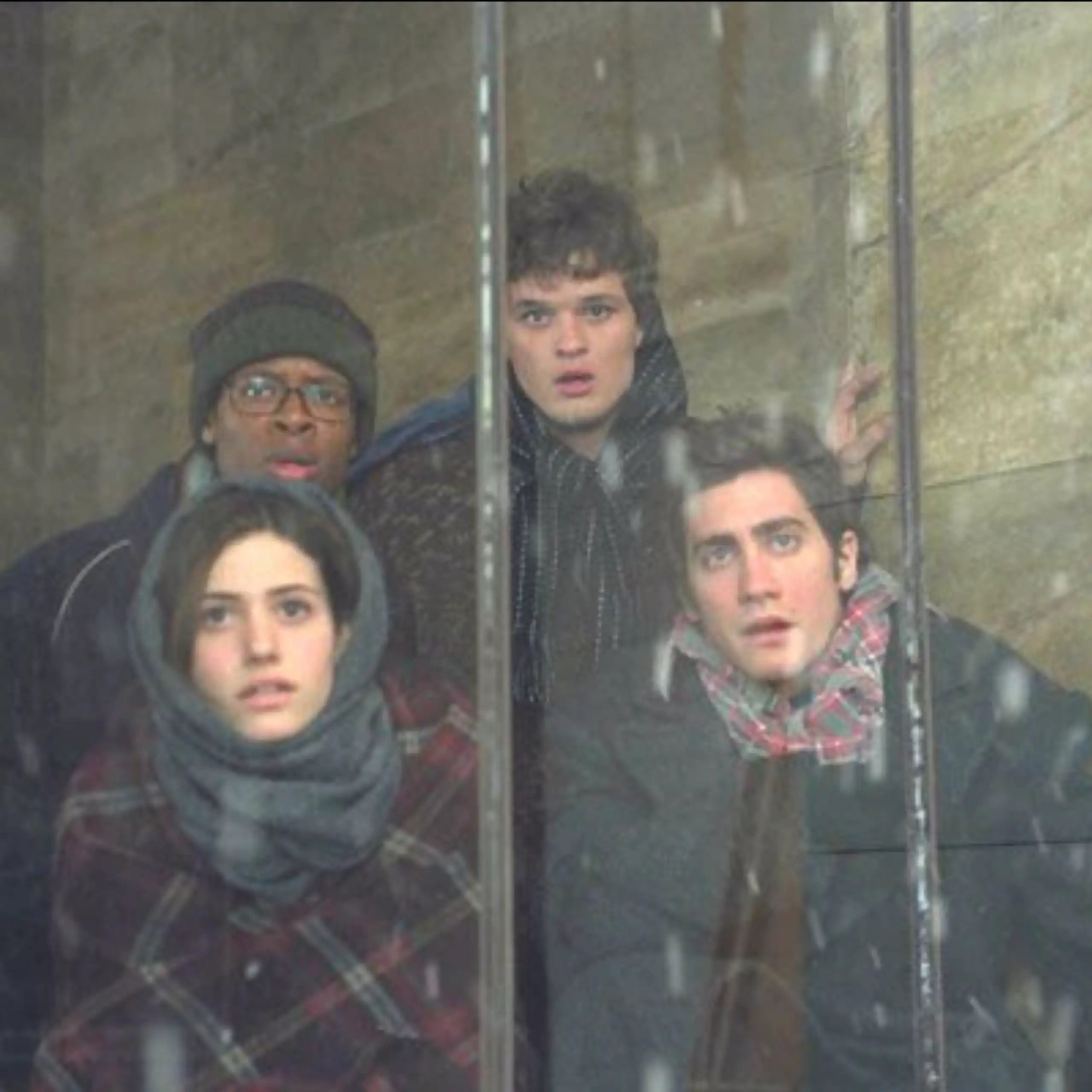 Quatre personnages du film regardent, tétanisés, à travers une baie vitrée.