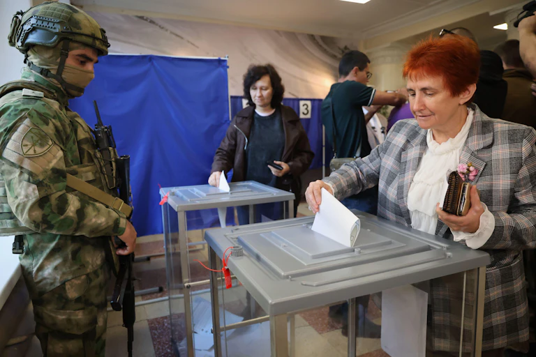 A Russian soldier watches as people cast their votes in a Russian-controlled part of the Donetsk region, Ukraine, Friday, Sept. 18, 2026.