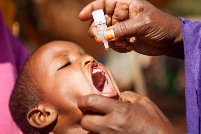 A young child with head tipped back and mouth open to receive drops from a small bottle held by an adult