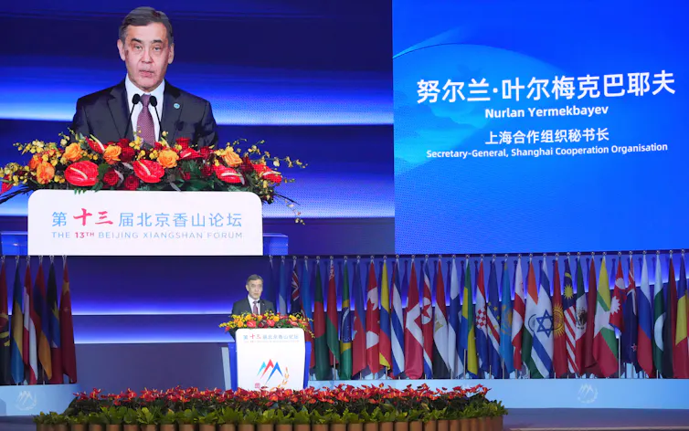 A man stands speaking at a podium festooned with flowers on a large stage.