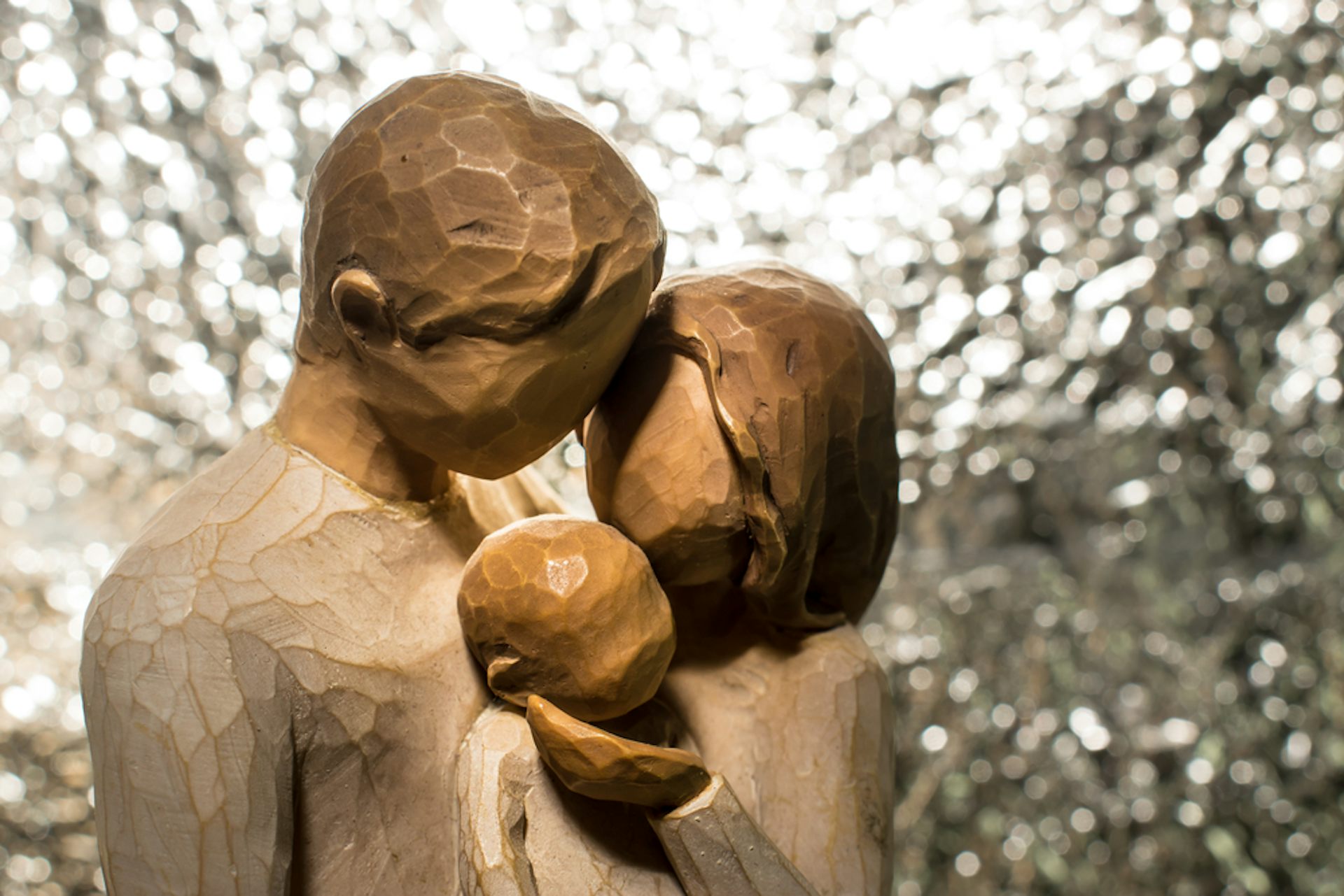 A wooden carving of a father, mother and baby embracing.