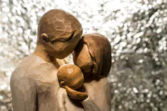 A wooden carving of a father, mother and baby embracing.