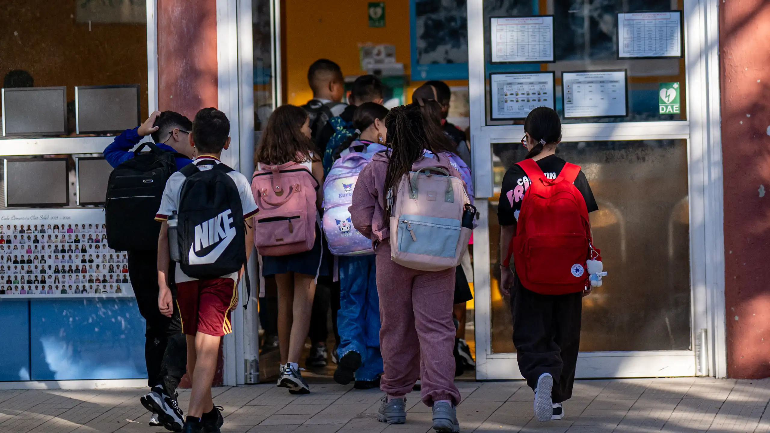 Des élèves entrent dans une salle de classe. Ils sont vus de dos.