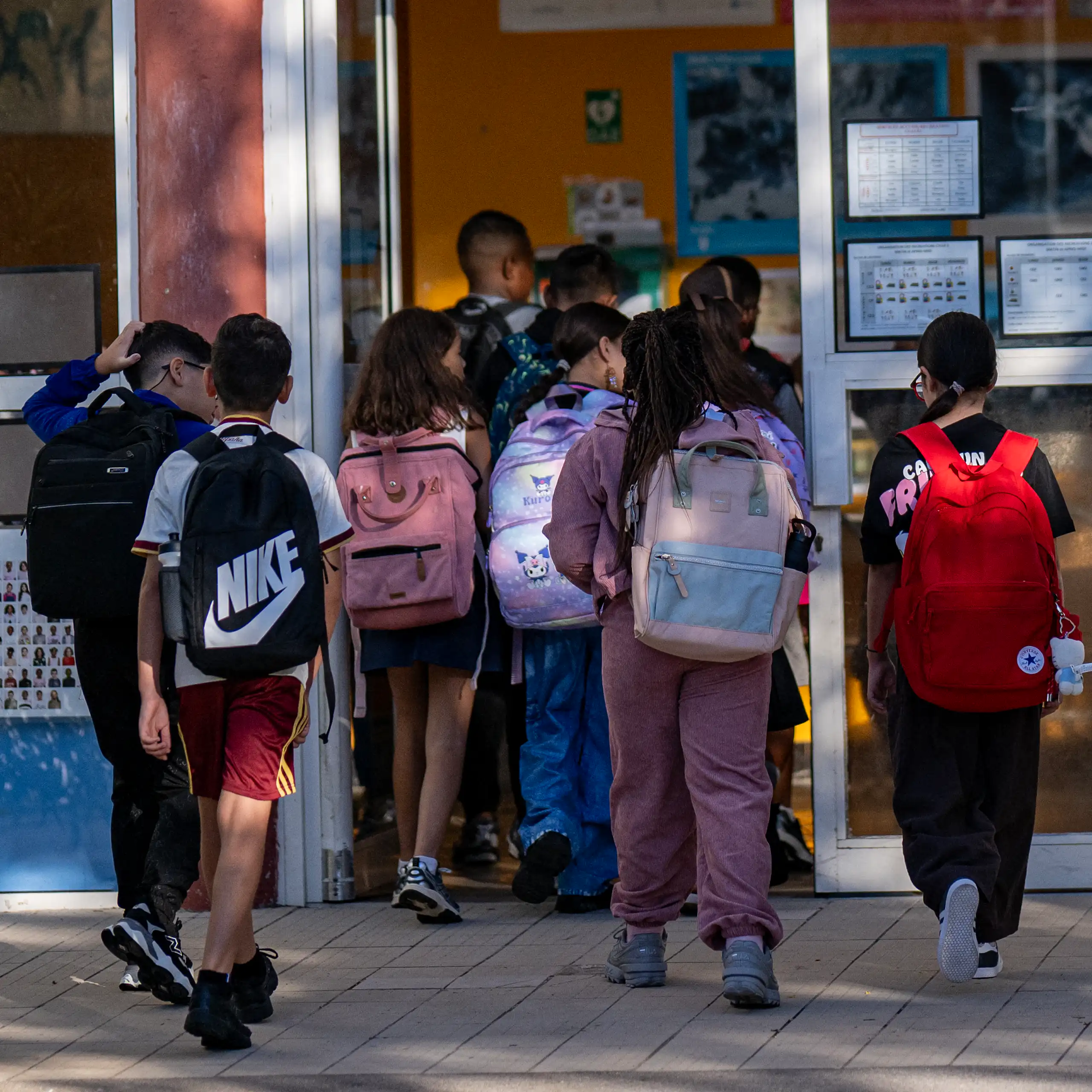 Des élèves entrent dans une salle de classe. Ils sont vus de dos.