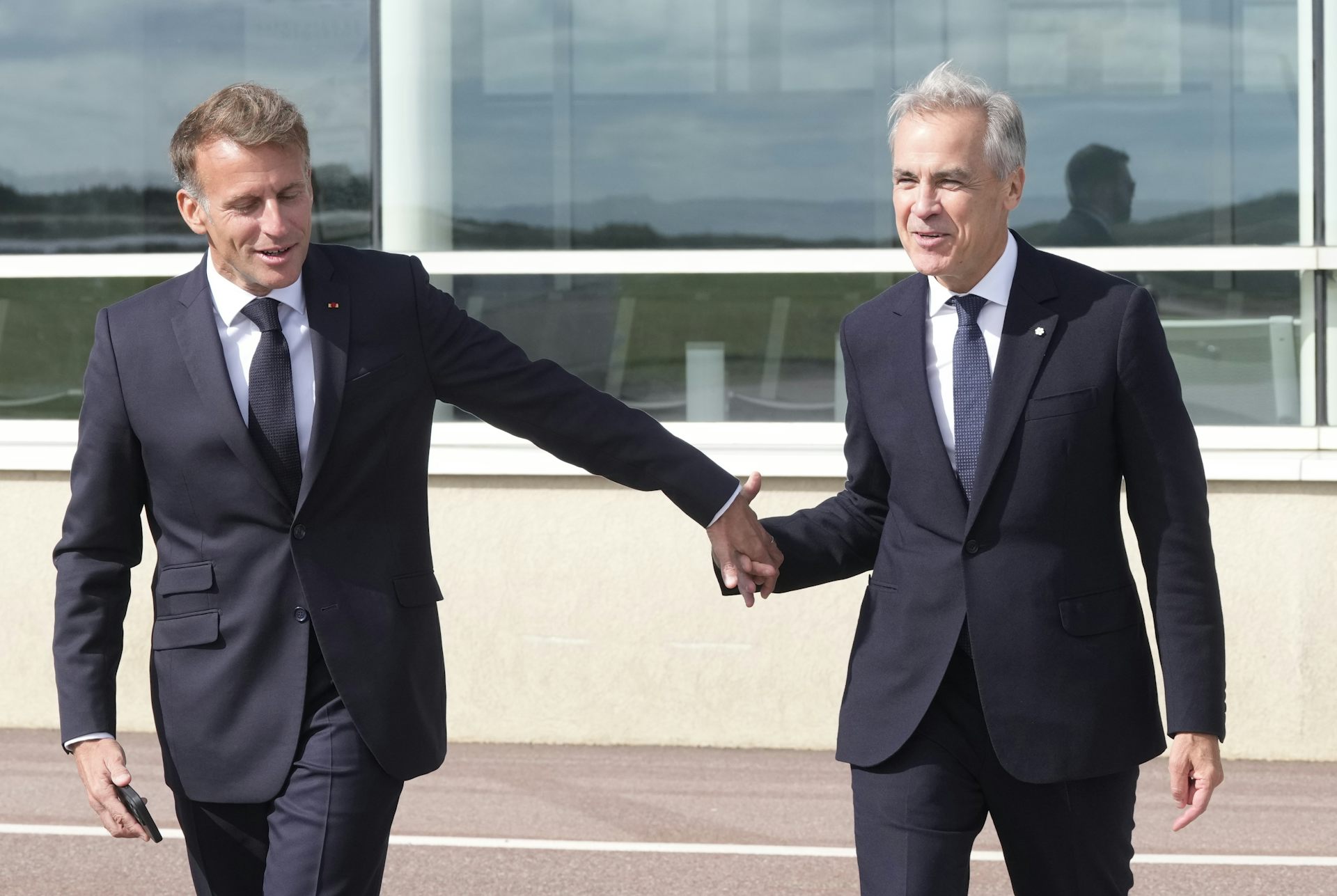Emmanuel Macron tient la main de Mark Carney, sur le tarmac d'un aéroport