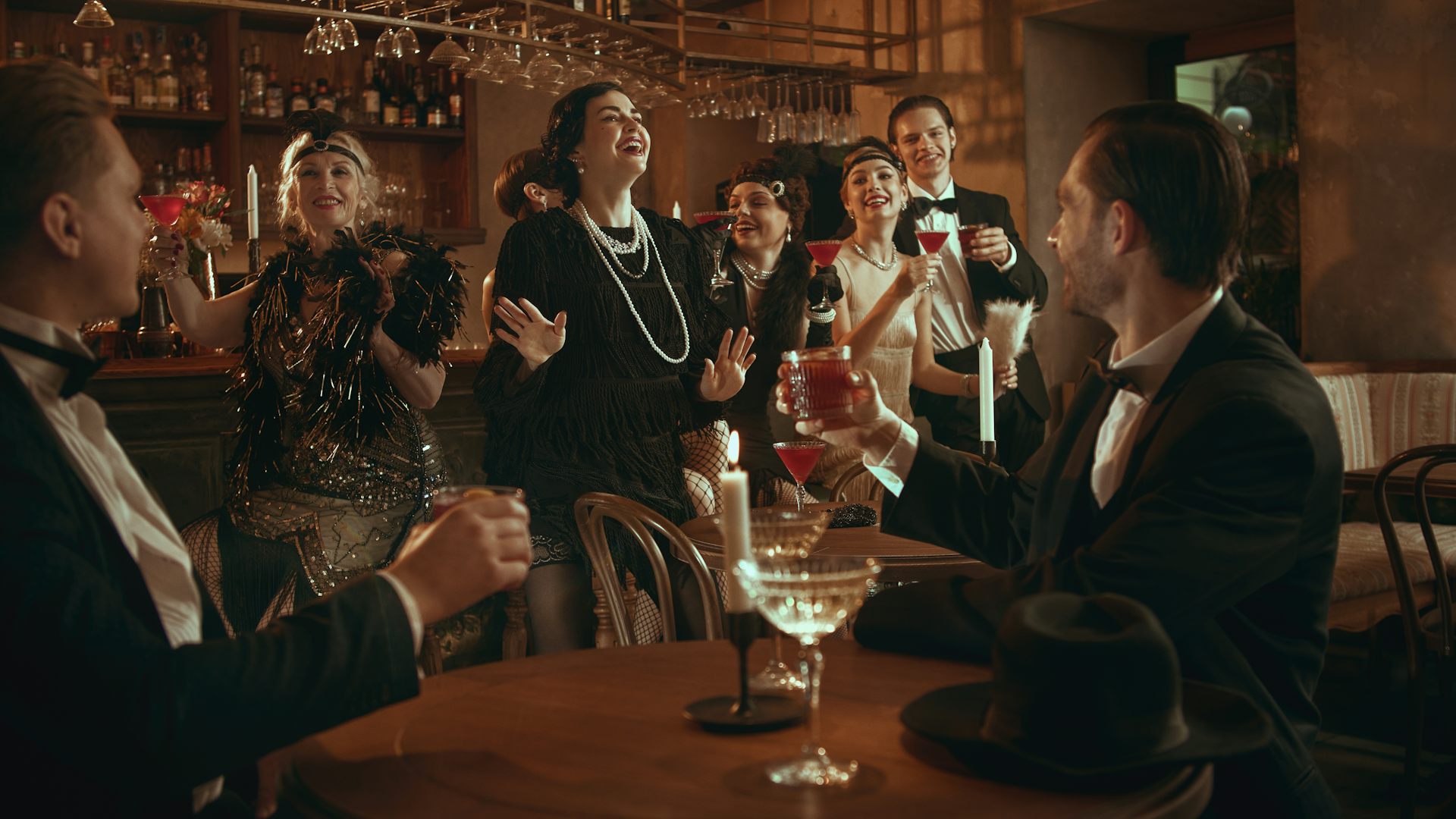 Um grupo de convidados de uma festa retrô rindo e comemorando enquanto bebem coquetéis.