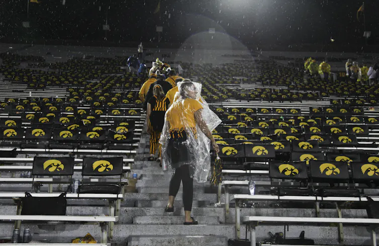 People with raincoats over their heads walk up stairs with Iowa Hawkeyes symbols on the seats around them.