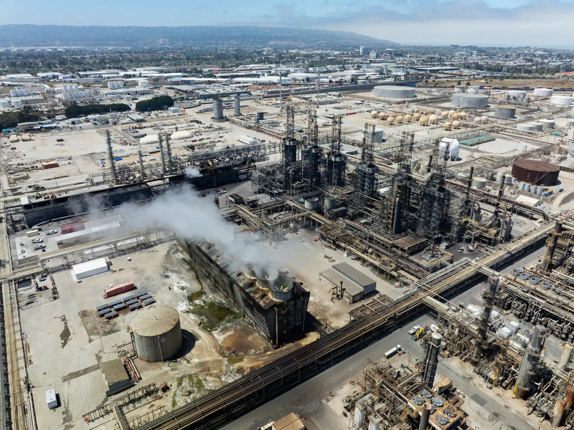 An aerial view shows an industrial site with tanks and pipes and smokestacks.