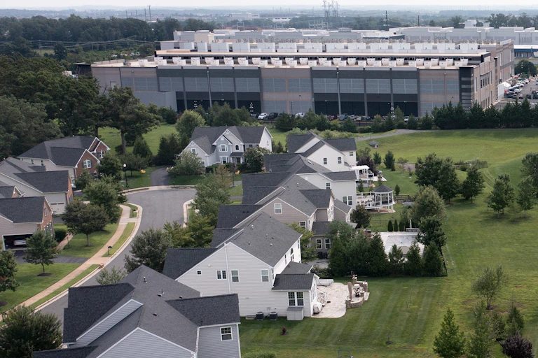 An aerial photo shows a residential neighborhood directly adjacent to a large data center building.