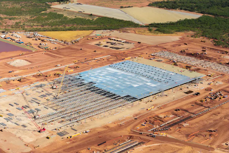 A large area of dirt has metal structures and cranes on it.