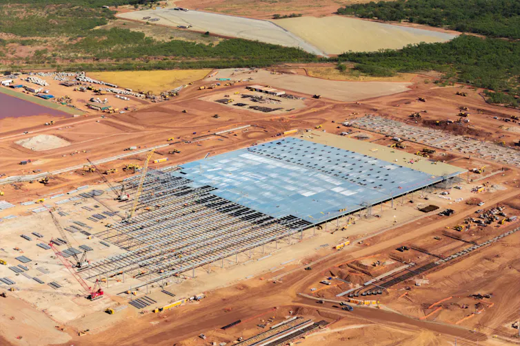 A large area of dirt has metal structures and cranes on it.