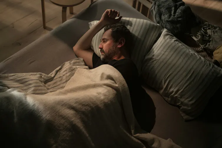 A man lies in bed in a dark room