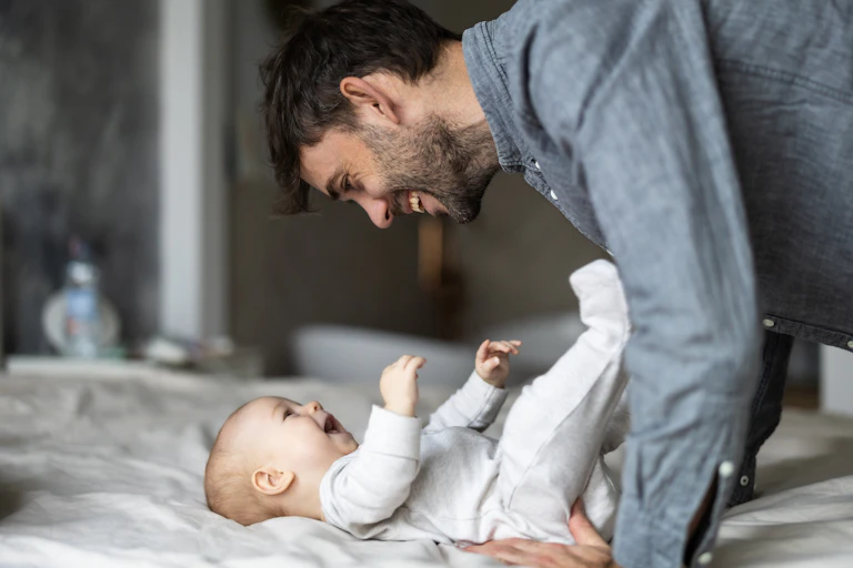 a father smiling down at his infant as the infant smiles back