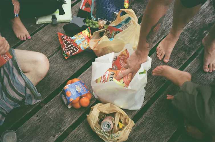 People sitting around bags of chips and other snacks, with only their hands and feet visible