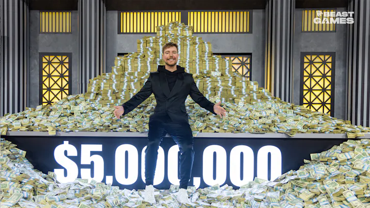 A man in a black suit sits in front of a giant piles of bash