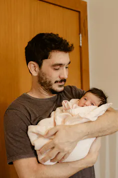 A man is holding a swaddled infant in his arms.