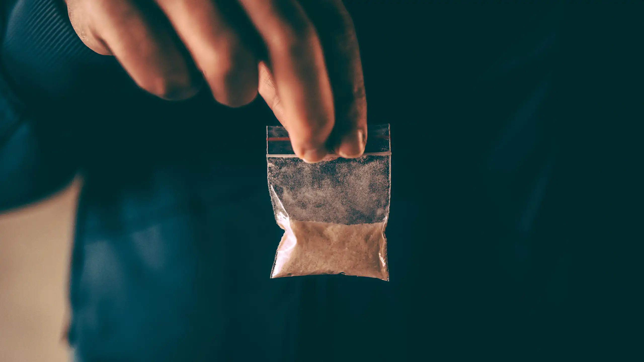Man holding small plastic bag of brown powder.