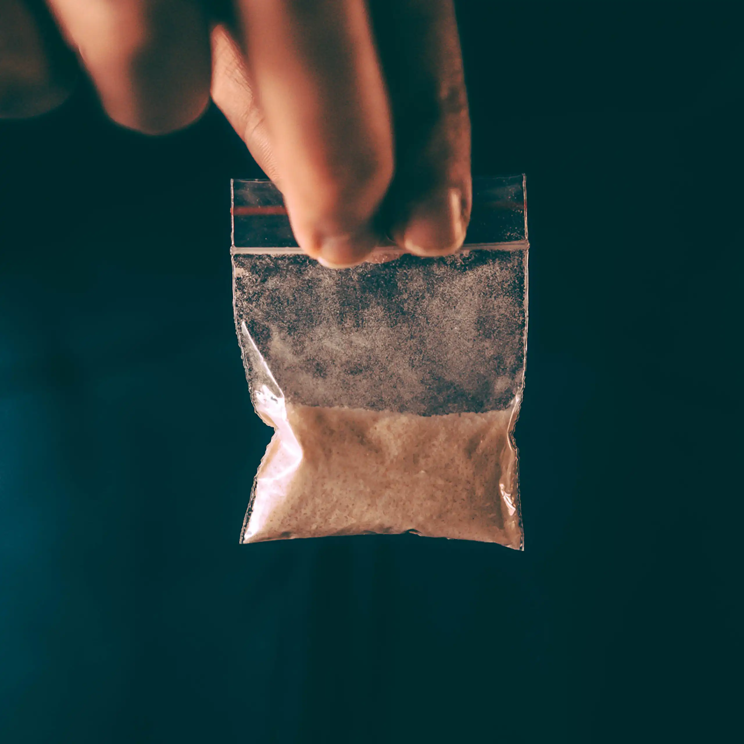 Man holding small plastic bag of brown powder.