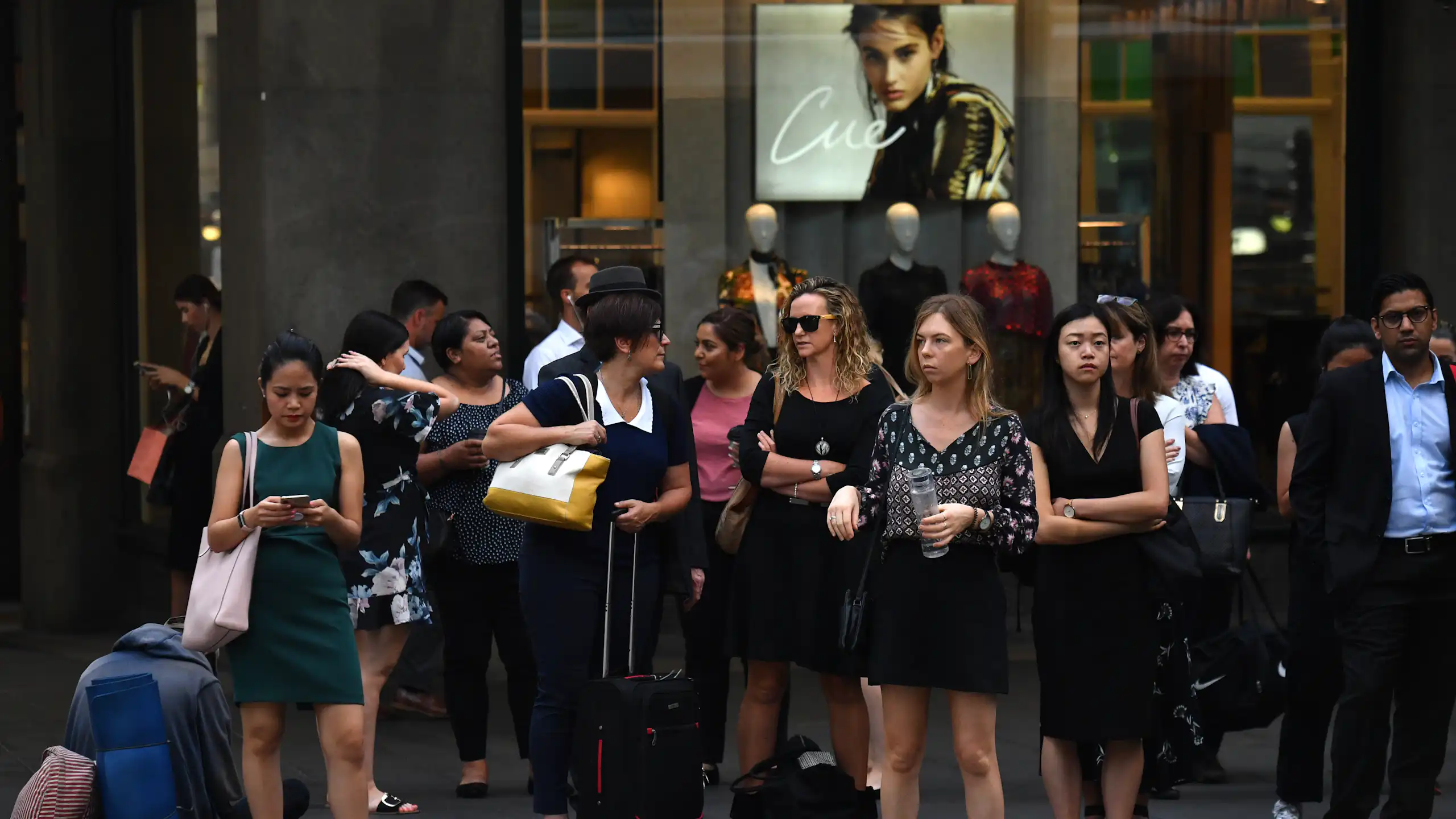 Women in office wear wait at traffic lights.
