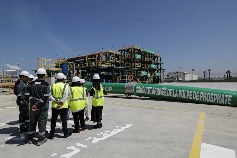 People in hard hats and yellow reflective vests stand next to a long green pipeline that says phosphate on it