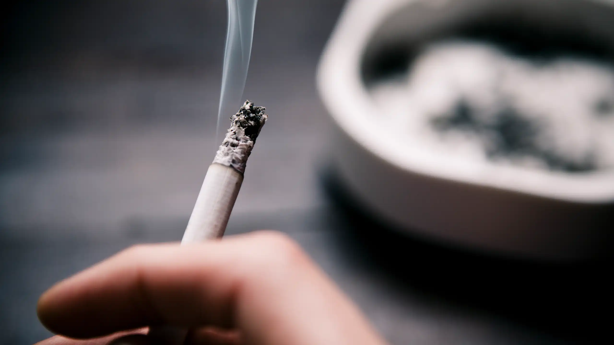 A close up of a hand holding a smoking cigarette