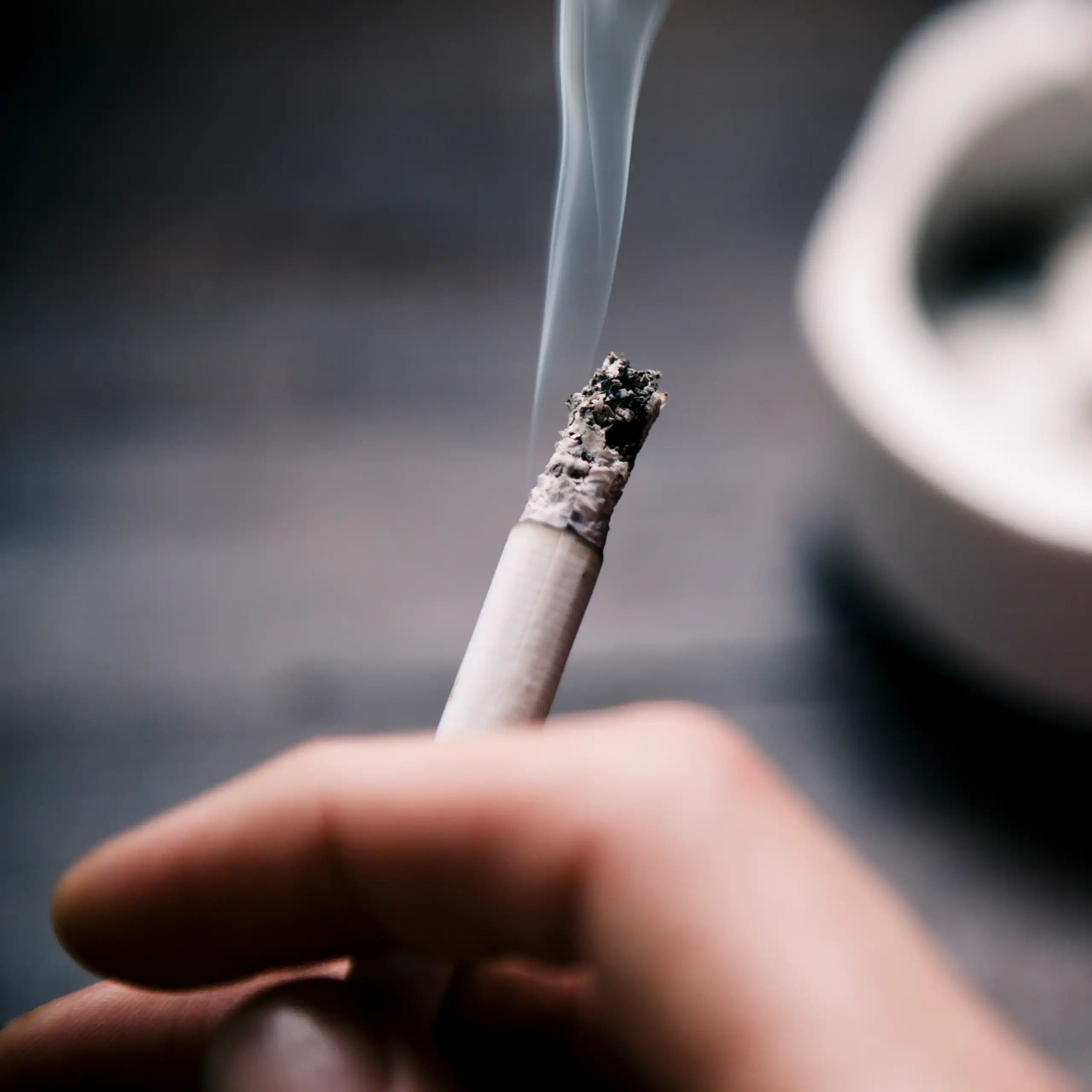 A close up of a hand holding a smoking cigarette