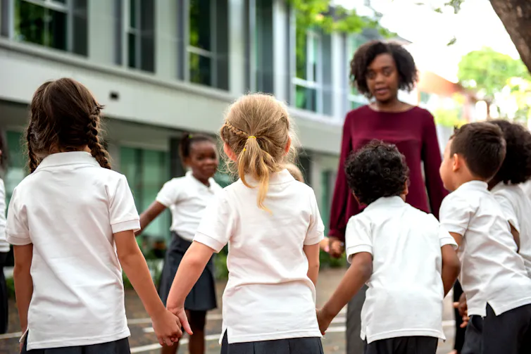 A group of schoolchildren outside holding hands, with their teacher