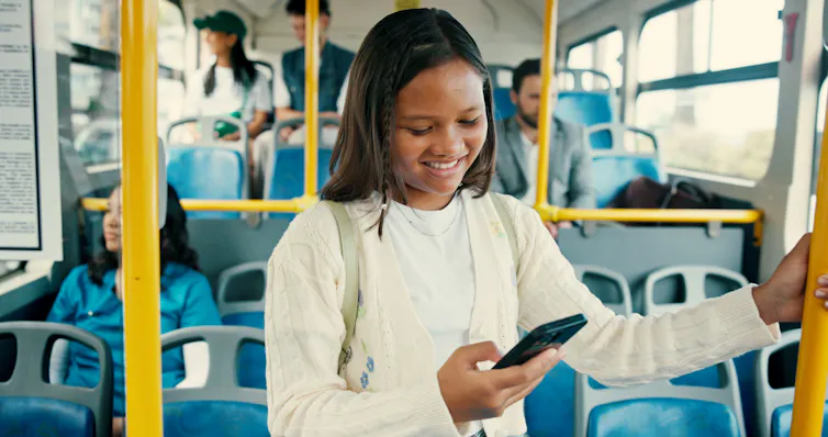 Young girl on bus smiling at her phone