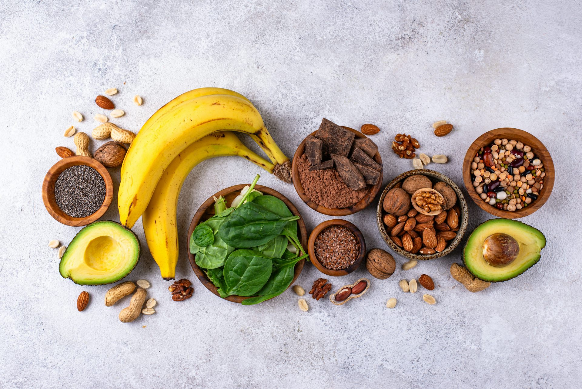An arrangement of magnesium-rich foods, including bananas, spinach, avocado and nuts.