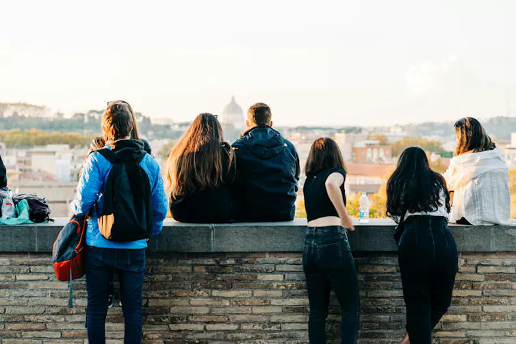 young people sit on a stone wall in a european city