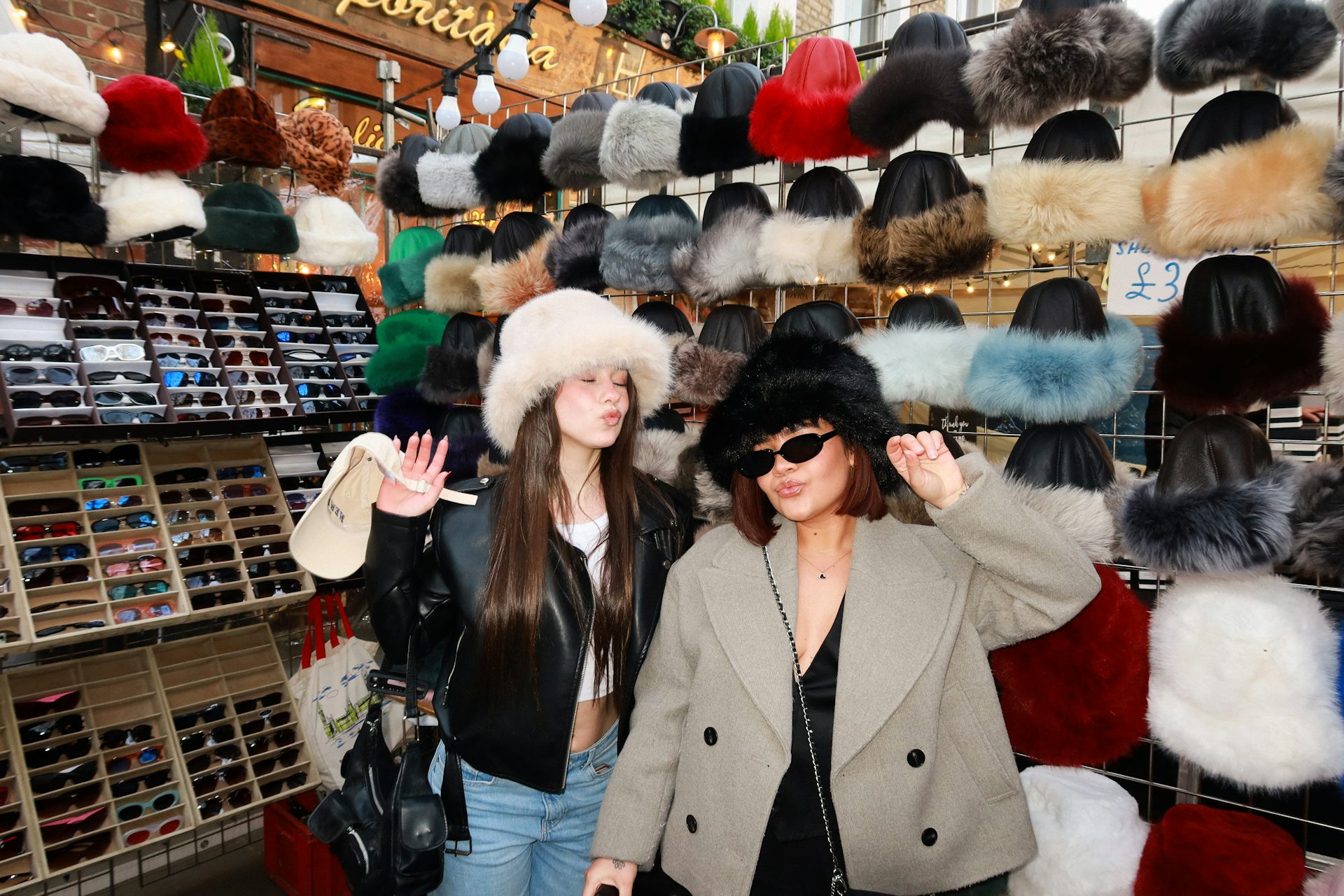 Two girls trying on fluffy hats at a market
