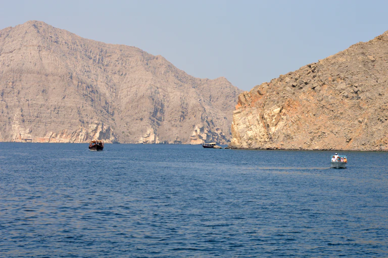 Boats sail through a stretch of sea between rocky cliffs.