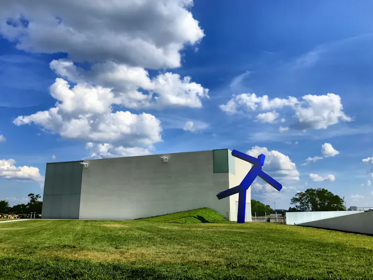 An abstract geometric blue sculpture on a lawn.
