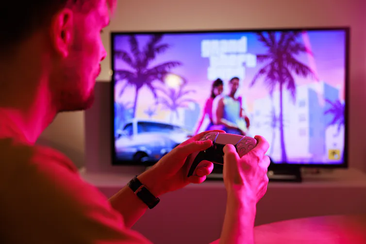 rear view of young man holding a controller and playing grand theft auto