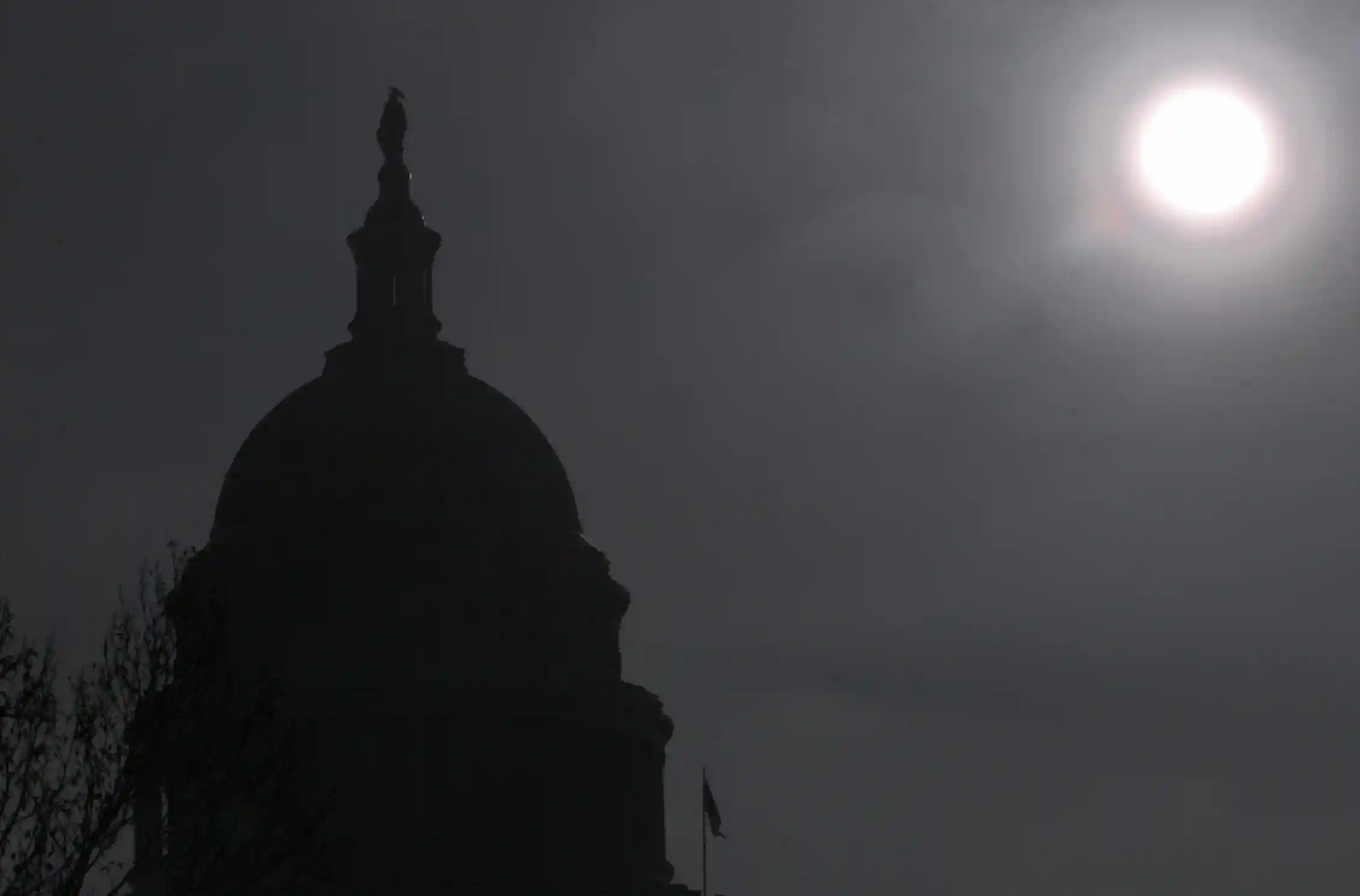 A black-and-white image shows the sun shining on a domed building.