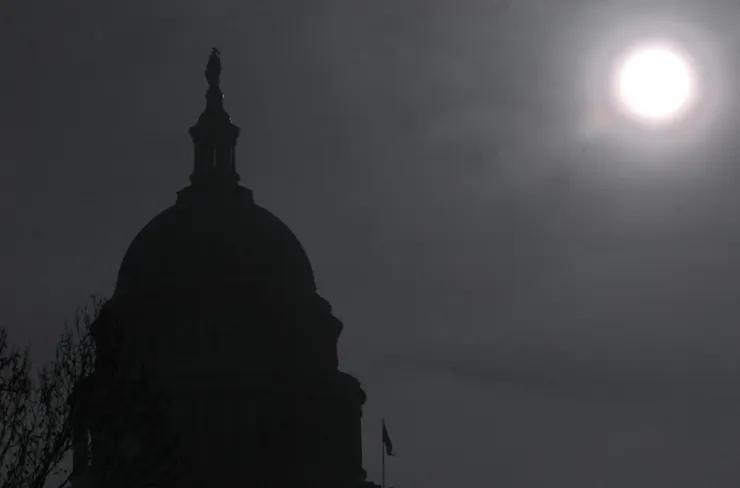 A black-and-white image shows the sun shining on a domed building.