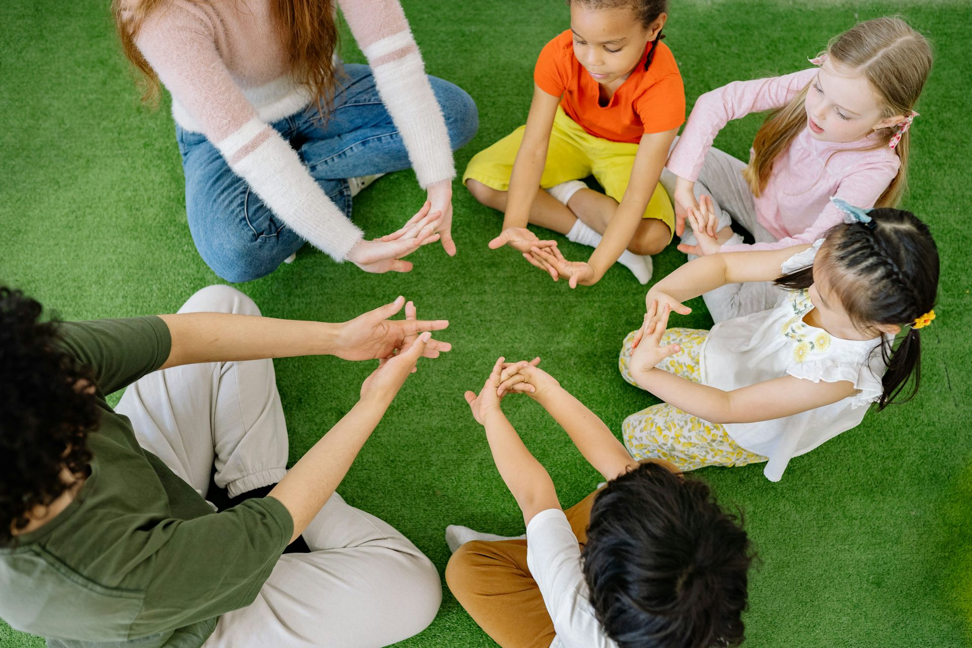 Children sitting in a circle, all making a hand pattern. 