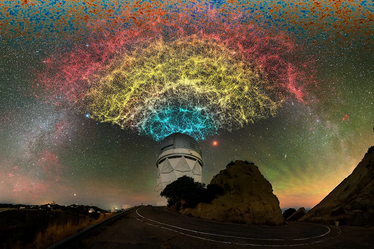 A dome telescope on top of a hill, the sky above illuminated with stars and yellow, blue and red light.