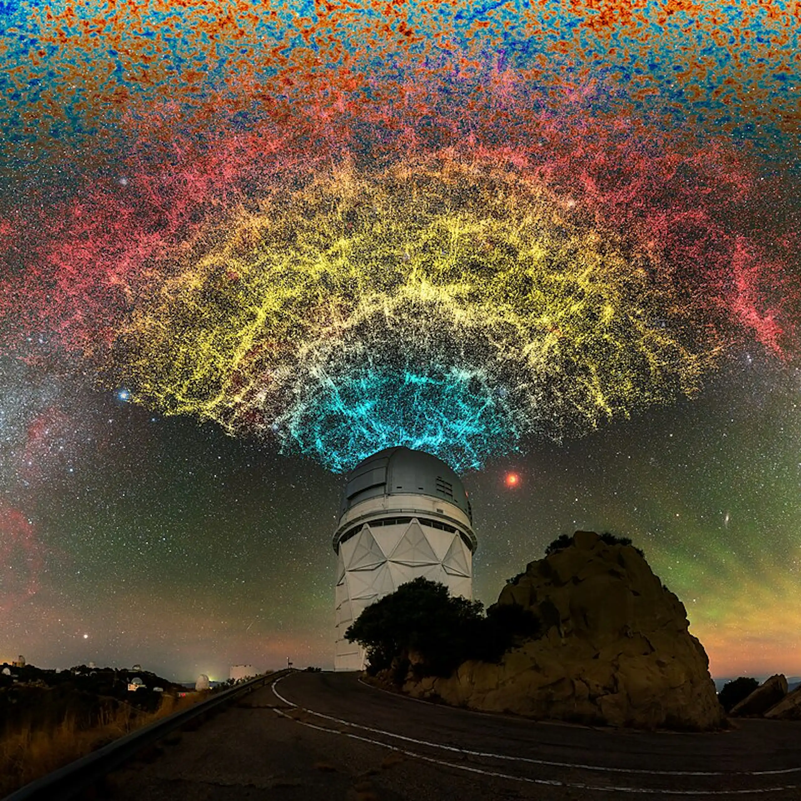 A dome telescope on top of a hill, the sky above illuminated with stars and yellow, blue and red light.
