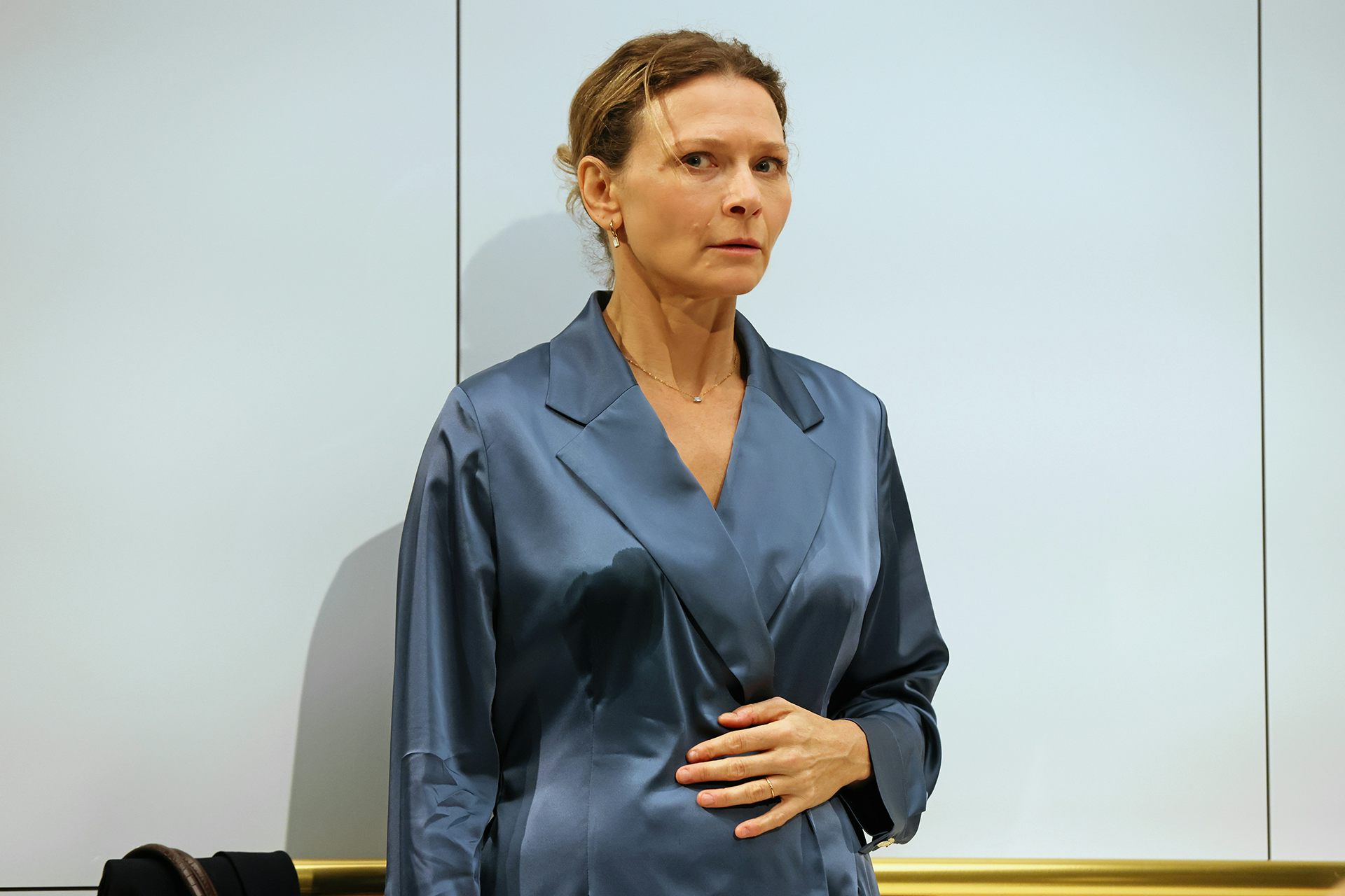 A woman in a blue silk blouse standing against an elevator wall, looking wary.