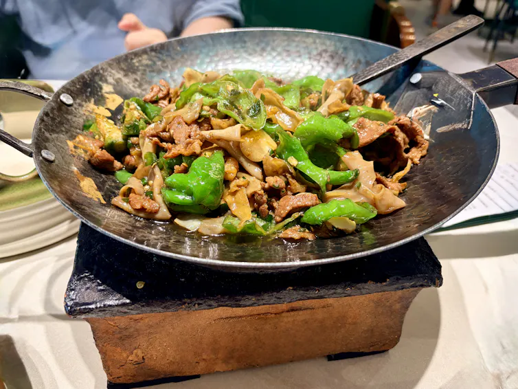 Sizzling beef and green peppers in a wok served at the table.