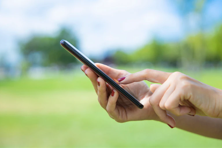 green grass in background, woman's hands hold smartphone