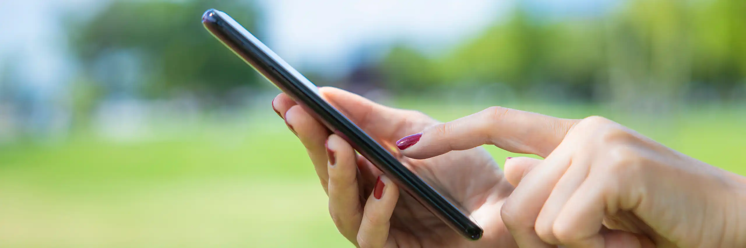 green grass in background, woman's hands hold smartphone