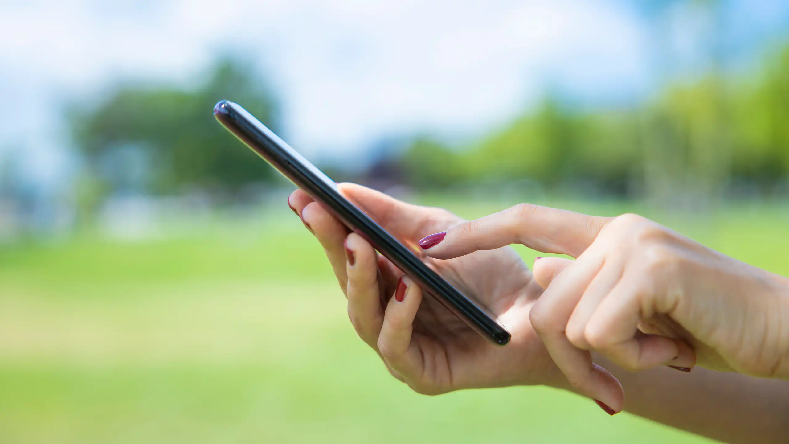 green grass in background, woman's hands hold smartphone