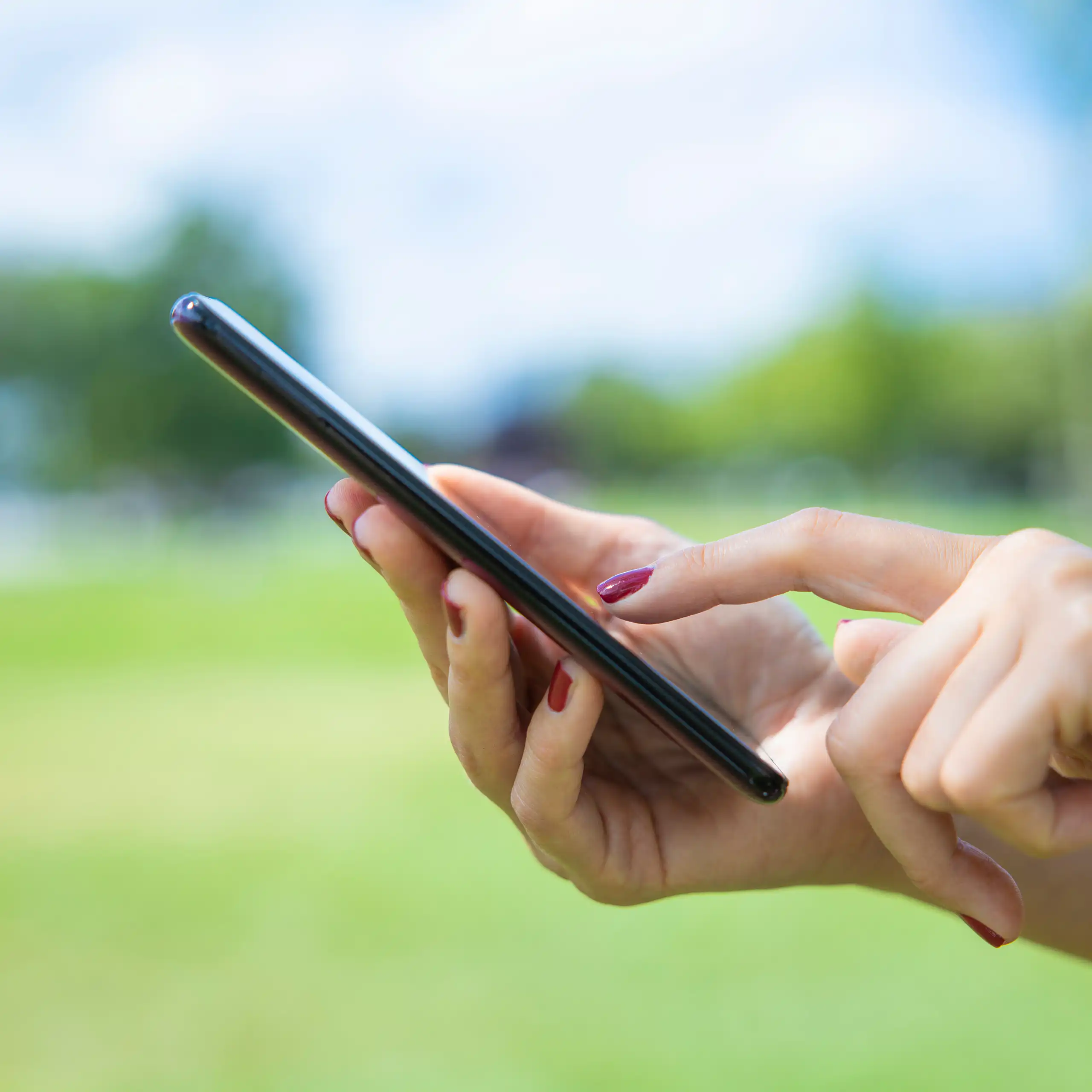 green grass in background, woman's hands hold smartphone