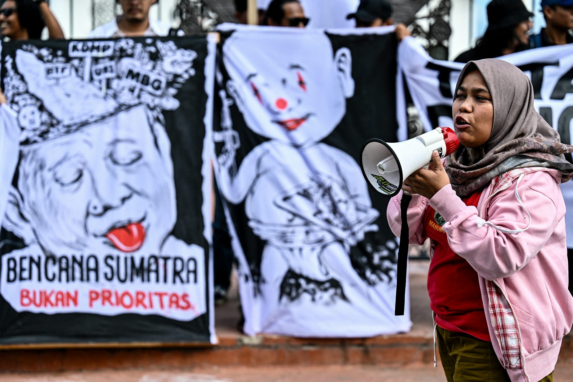 A woman with a megaphone stands in front of posters.
