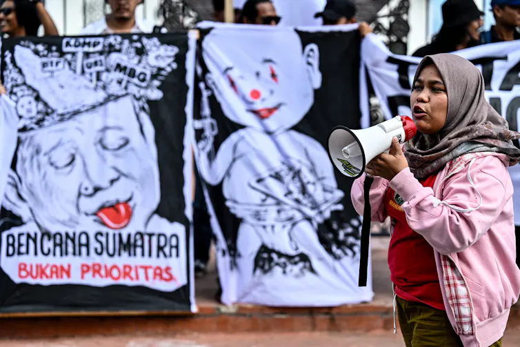 A woman with a megaphone stands in front of posters.