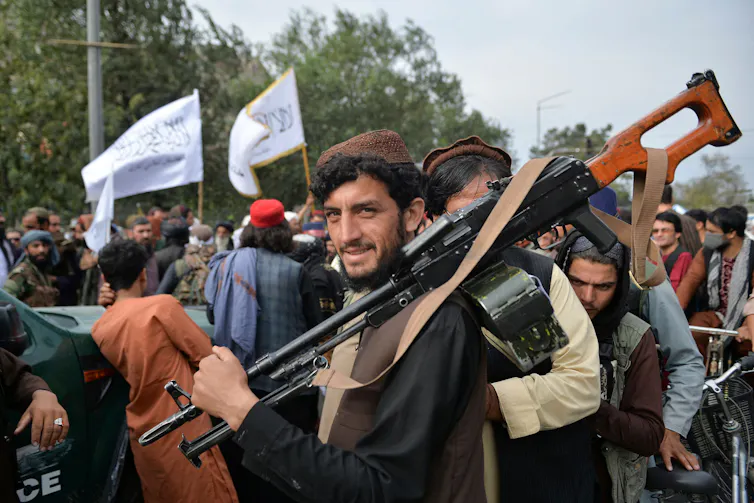 A man holds a large gun while white flags fly in the background.