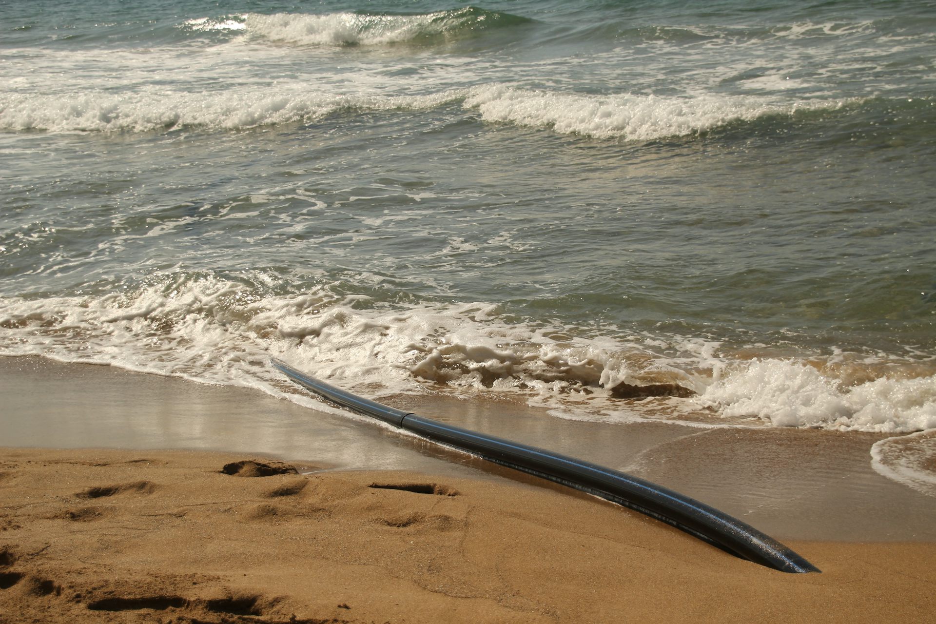 Gros plan sur le câble émergeant du sable et plongeant dans la mer.