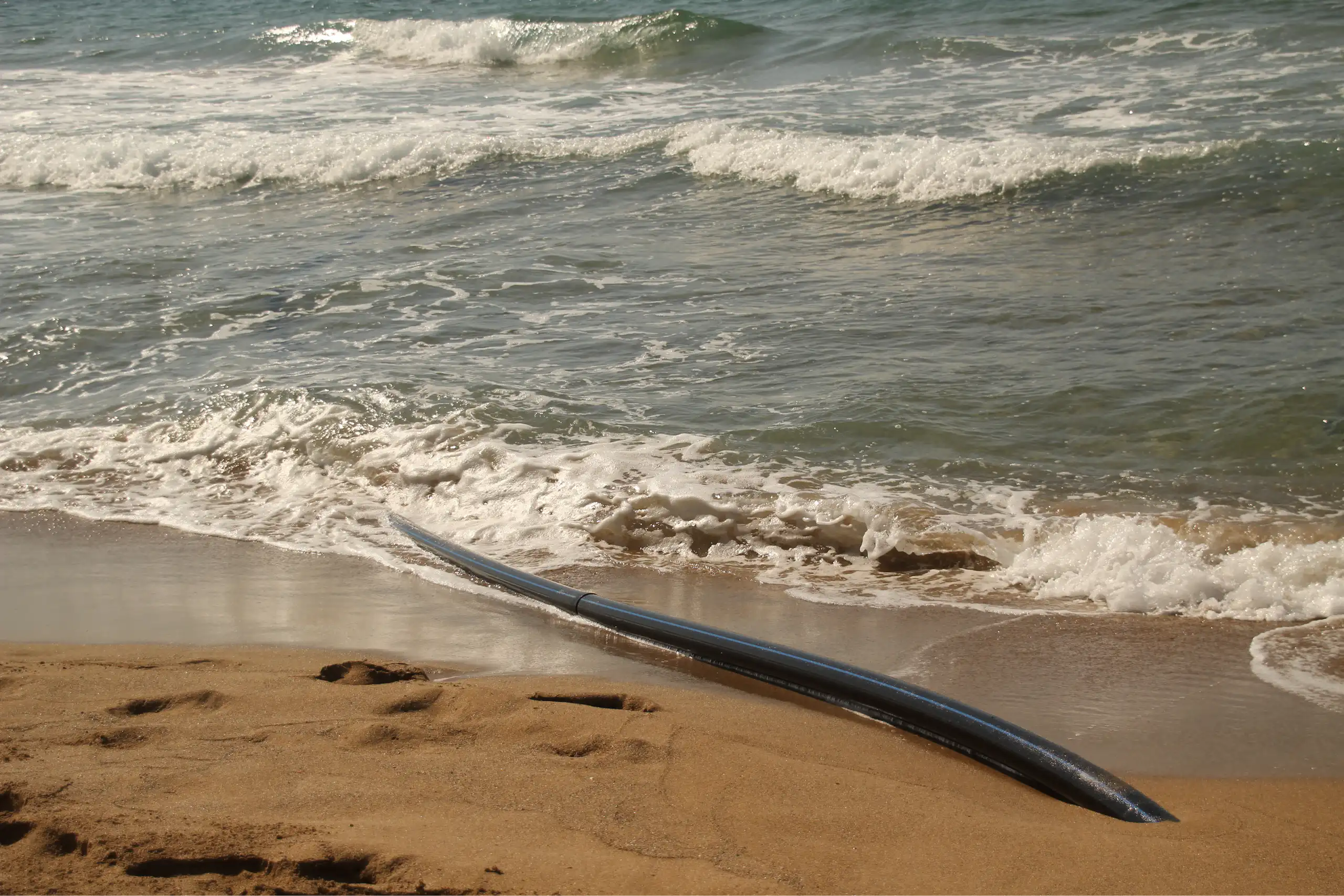 Gros plan sur le câble émergeant du sable et plongeant dans la mer.